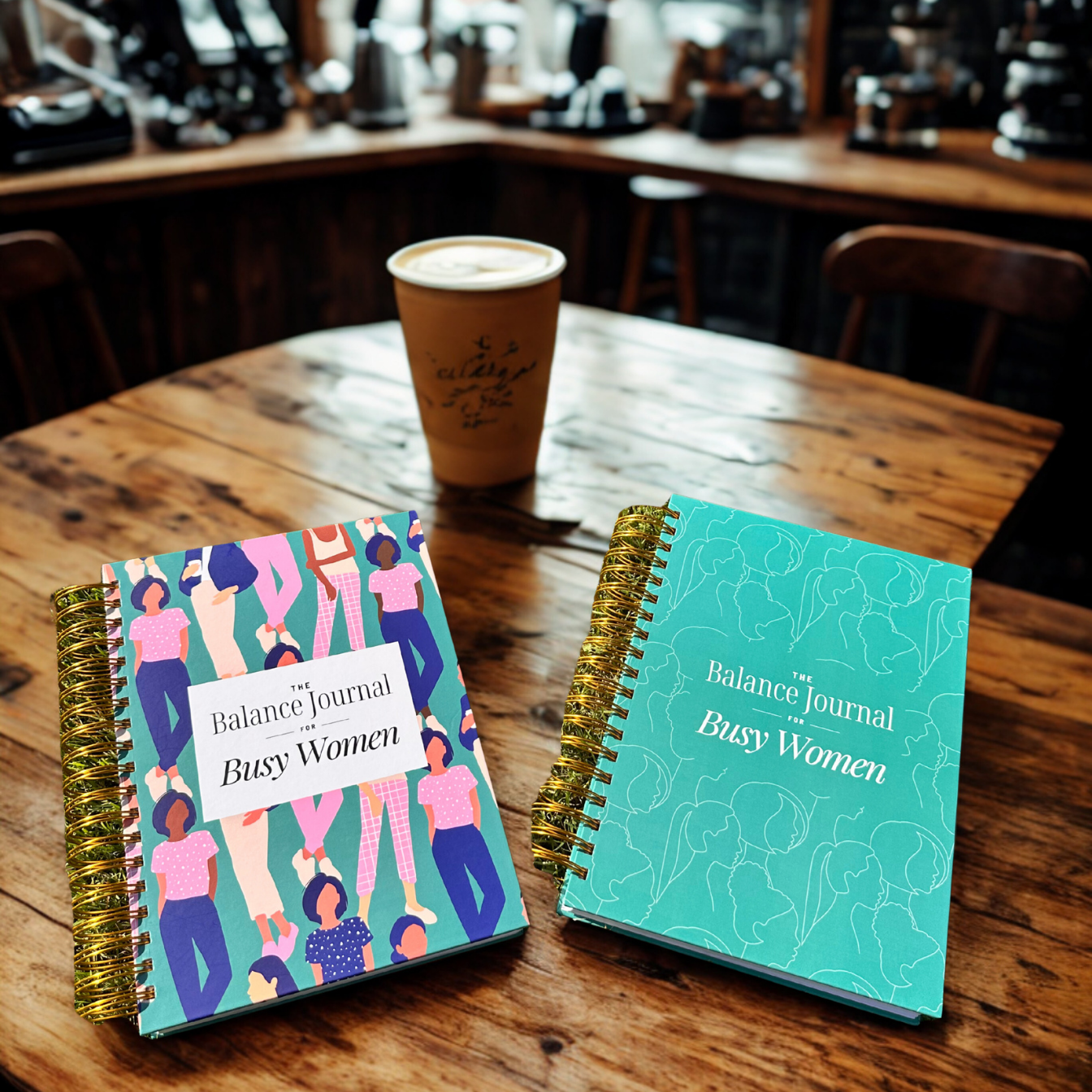 Two 'Balance Journal for Busy Women' on a wooden table with a coffee cup in the background.
