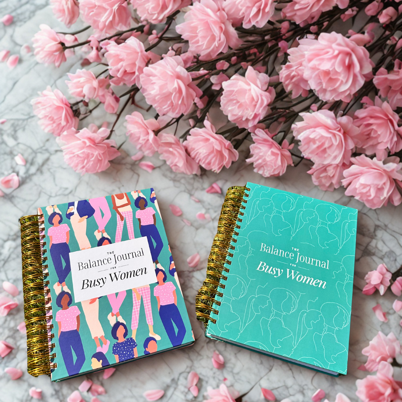 Two journals titled 'The Balance Journal for Busy Women' on a surface with pink flowers.