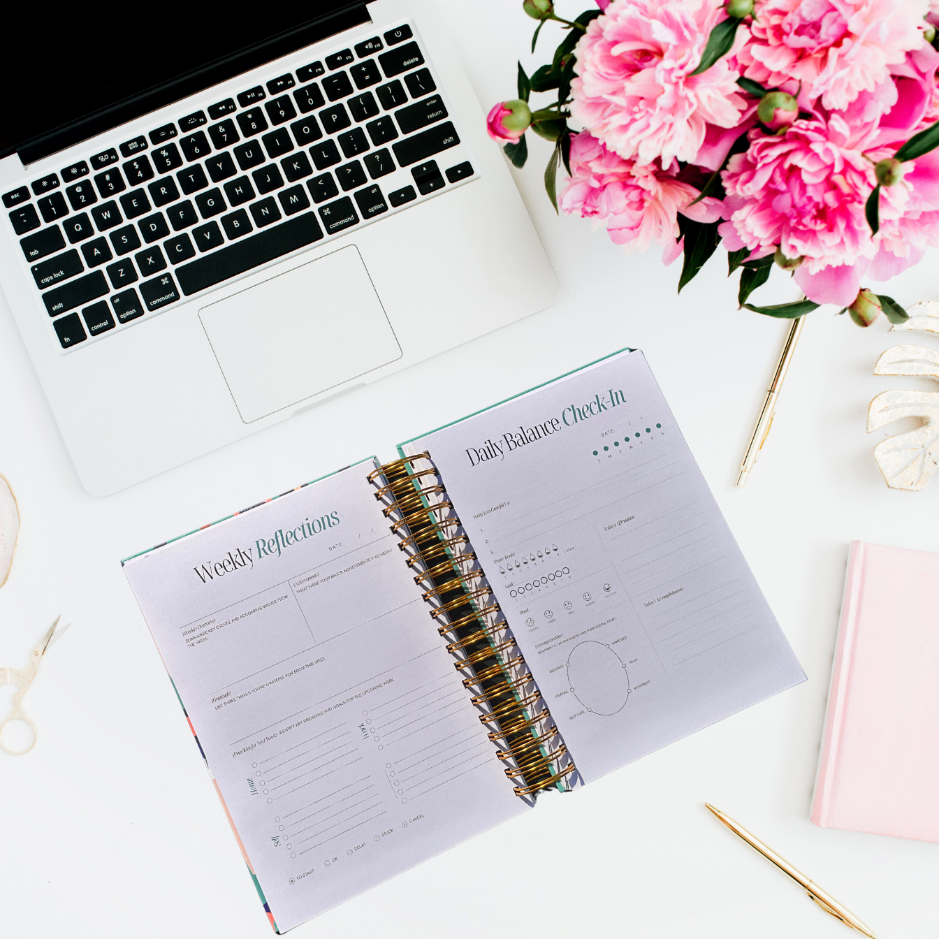 Open planner with weekly reflections section on a desk with a laptop and pink flowers.